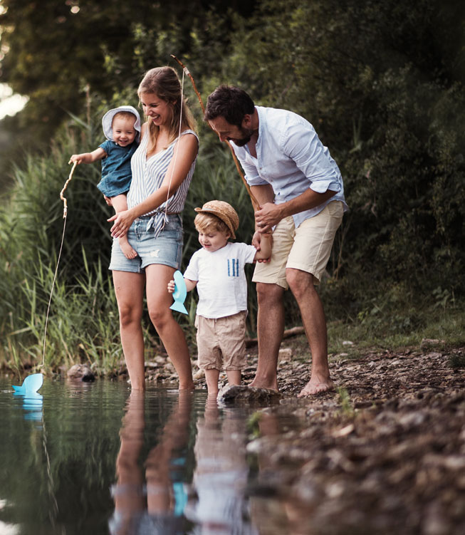 A young family with two toddler children outdoors by the river in summer